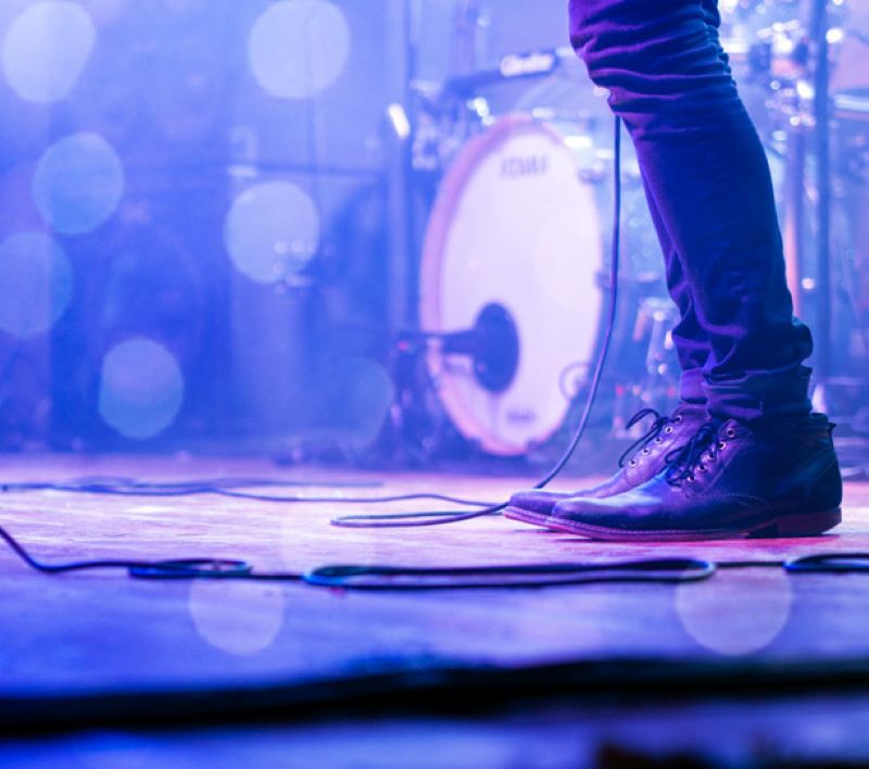 A close up photograph of a pair of legs on a stage with a drumkit in the background