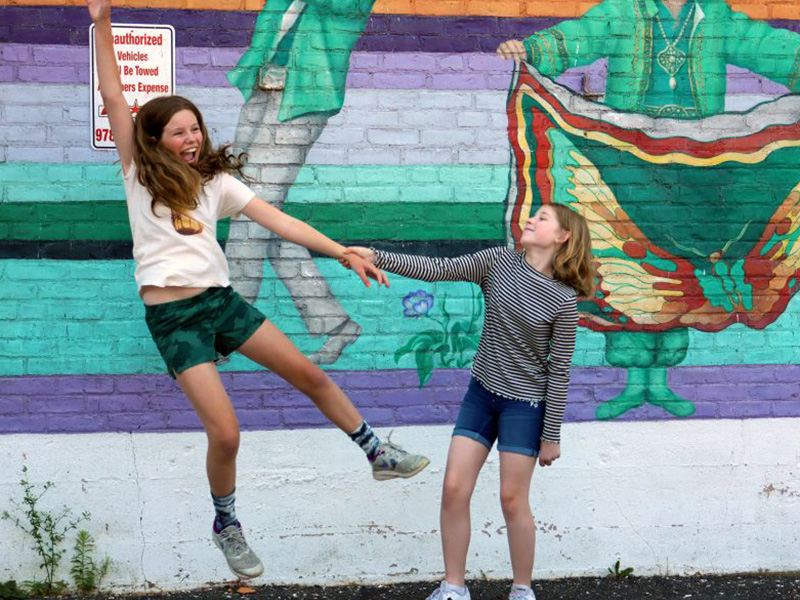 A photograph of two girls jumping in front of a mural.
