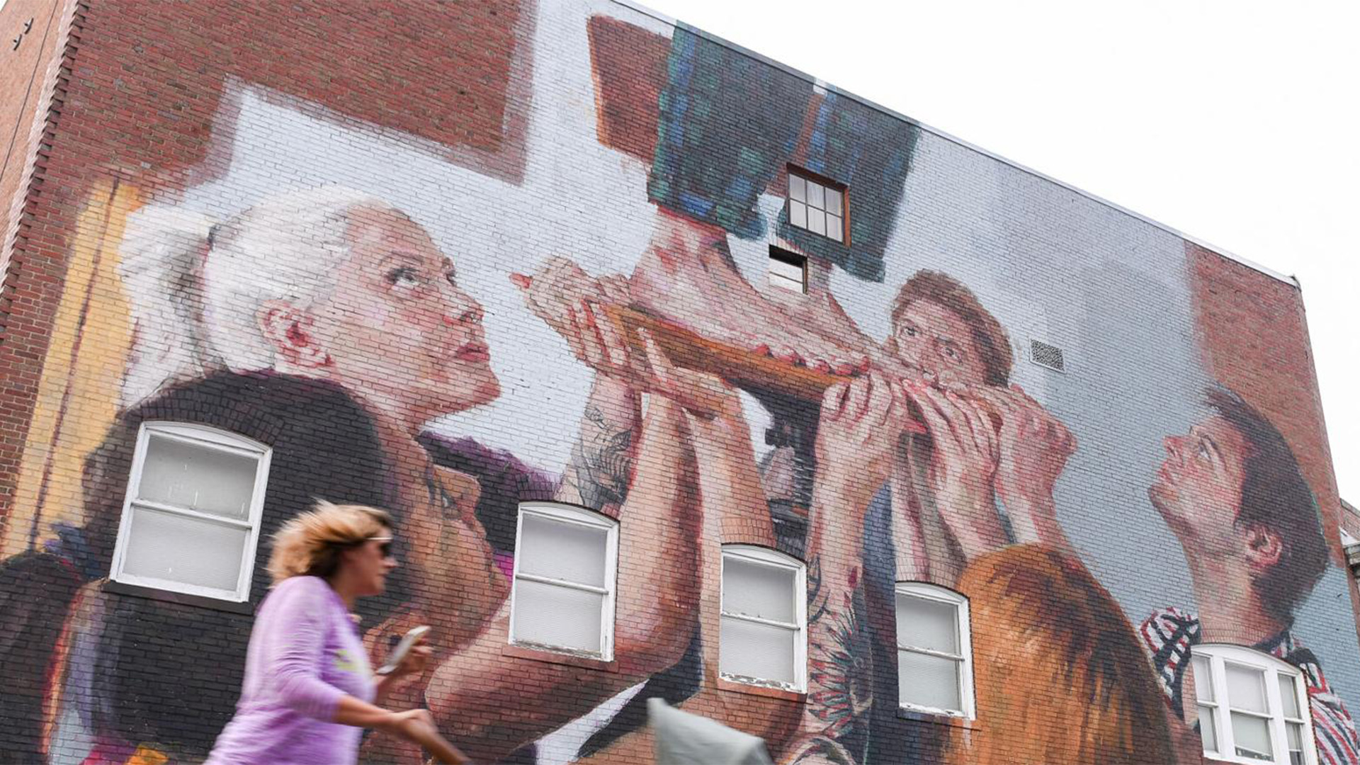 A mural outside of The Cabot featuring a group of people holding another person up.